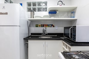 A kitchen with white cabinets, a black countertop, a stainless steel sink, a microwave, and a refrigerator. - Fully Equipped Apartments in the Best Location Just Steps From the sea in Guarapari - STP (Guarapari)