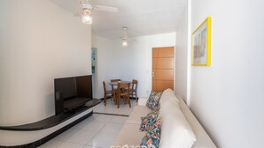 A living room with a sofa, TV, ceiling fan, and dining table. - Fully Equipped Apartments in the Best Location Just Steps From the sea in Guarapari - STP (Guarapari)
