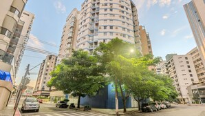 A multi-story residential building with balconies, a tree-lined street, and parked cars. - Fully Equipped Apartments in the Best Location Just Steps From the sea in Guarapari - STP (Guarapari)