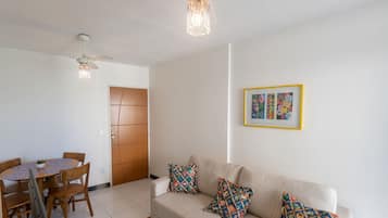 Una sala de estar con un sofá color beige, cojines estampados, una mesa de comedor con sillas y un ventilador de techo.
