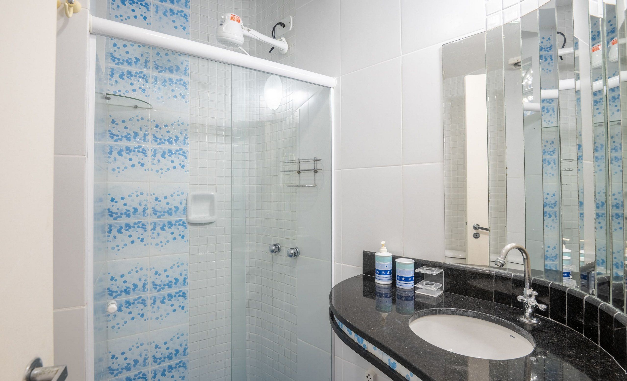 Un baño con ducha de vidrio, lavamanos con encimera negra y espejo.