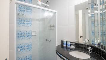 Un baño con ducha de vidrio, lavamanos con encimera negra y espejo.