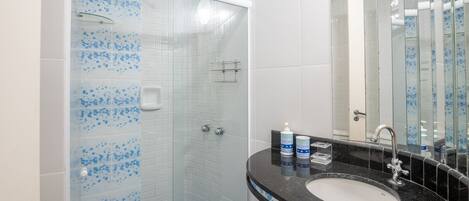 A bathroom with a glass-enclosed shower, a black countertop sink, and a mirror.