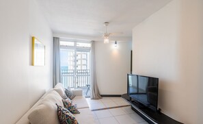 A modern living room with a sofa, TV, and a balcony view. - Fully Equipped Apartments in the Best Location Just Steps From the sea in Guarapari - STP (Guarapari)