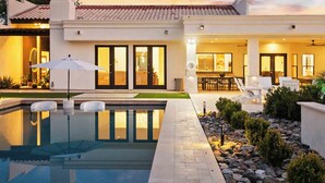 Una casa moderna con piscina, mobiliario exterior y un patio bien iluminado.