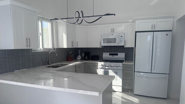 A modern kitchen with white cabinetry, a central island, a built-in oven, a microwave, and a refrigerator.