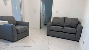A room with two grey sofas, a white table, and a marble floor.