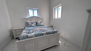 A bedroom with a bed, two nightstands, a dresser, and two windows.