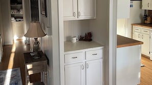 Una cocina compacta con muebles blancos, encimera de madera y un refrigerador visible.