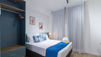 Quarto de hotel com cama, mesa de cabeceira, guarda-roupa e janela com cortinas.