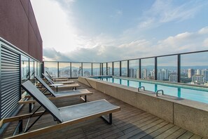 A rooftop pool with lounge chairs and a city view.