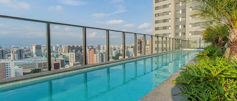 A rooftop infinity pool with a city view, surrounded by glass railings and greenery.