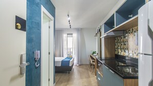A compact hotel room with a kitchenette, a bed with a blue blanket, a desk with a chair, and a bathroom with a toilet and sink. - Modern Studio Near Allianz Parque Sp-p2002b (São Paulo)