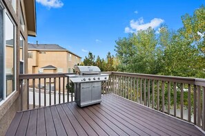 Une terrasse dotée d’un barbecue, d’une rambarde en bois et offrant une vue sur les maisons voisines.