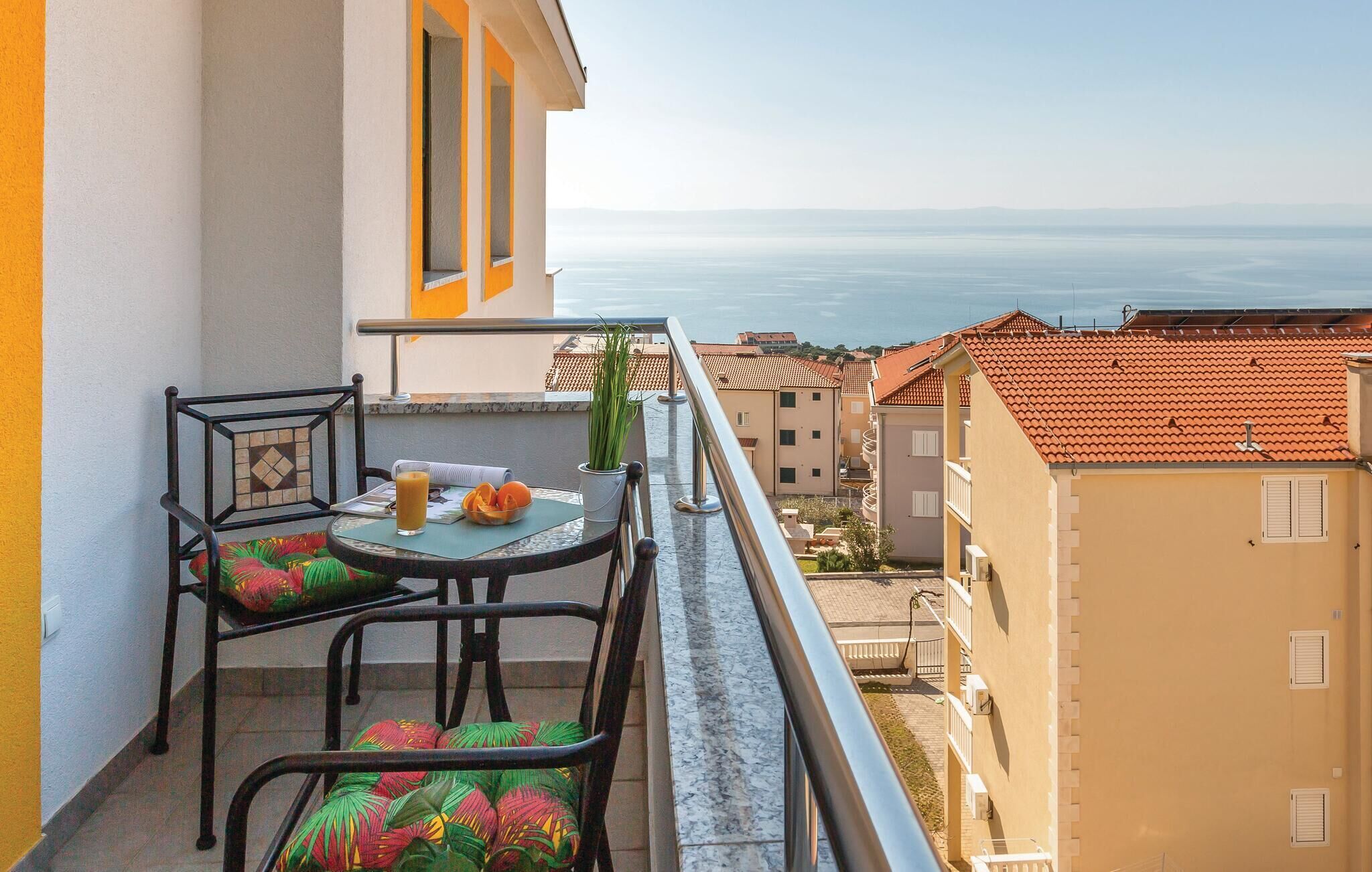 Ein Balkon mit Tisch und Stühlen, Blick aufs Meer und angrenzende Gebäude.