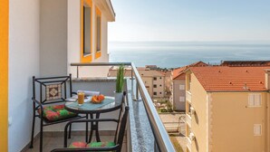 A balcony with a table and chairs, a view of the sea, and neighboring buildings.