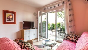 Una sala de estar con un televisor sobre un mueble bajo, una mesa de vidrio y un sofá con cojines estampados.