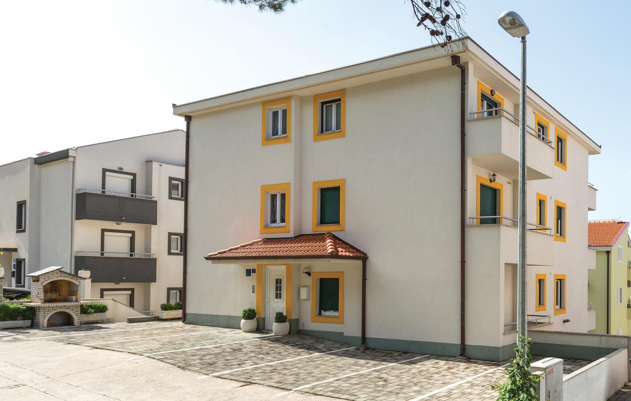 A multi-story residential building with a tiled roof, a small outdoor seating area, and a parking lot.