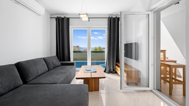 Un salon moderne avec un canapé, une table basse en bois et une vue sur une piscine, visible à travers de grandes portes vitrées.