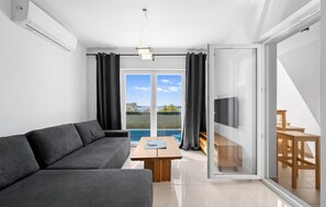 A modern living room with a sofa, a wooden coffee table, and a view of a swimming pool through large glass doors.