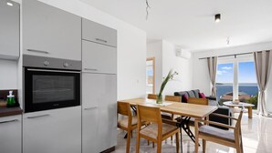 A modern kitchen with a built-in oven, a dining area with wooden furniture, and a view of the sea through large windows.