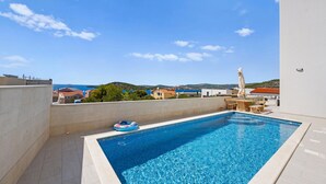 A rooftop swimming pool with a view of the sea and surrounding buildings.