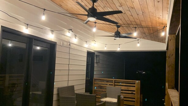 Una terraza al aire libre techada, con ventiladores de techo, luces colgantes y mobiliario de mimbre.