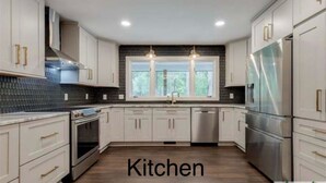 Una cocina moderna con armarios blancos, electrodomésticos de acero inoxidable y un protector contra salpicaduras negro.