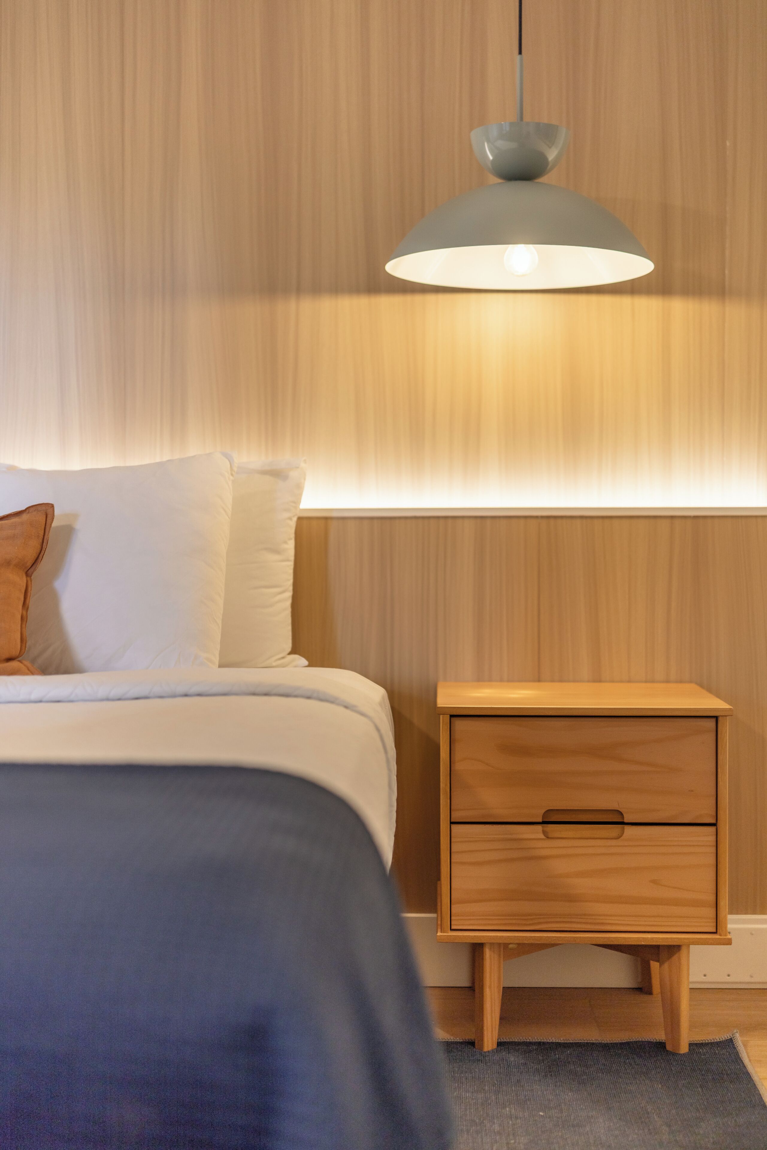 Et soveværelse med seng, natbord og en hængende lampe.