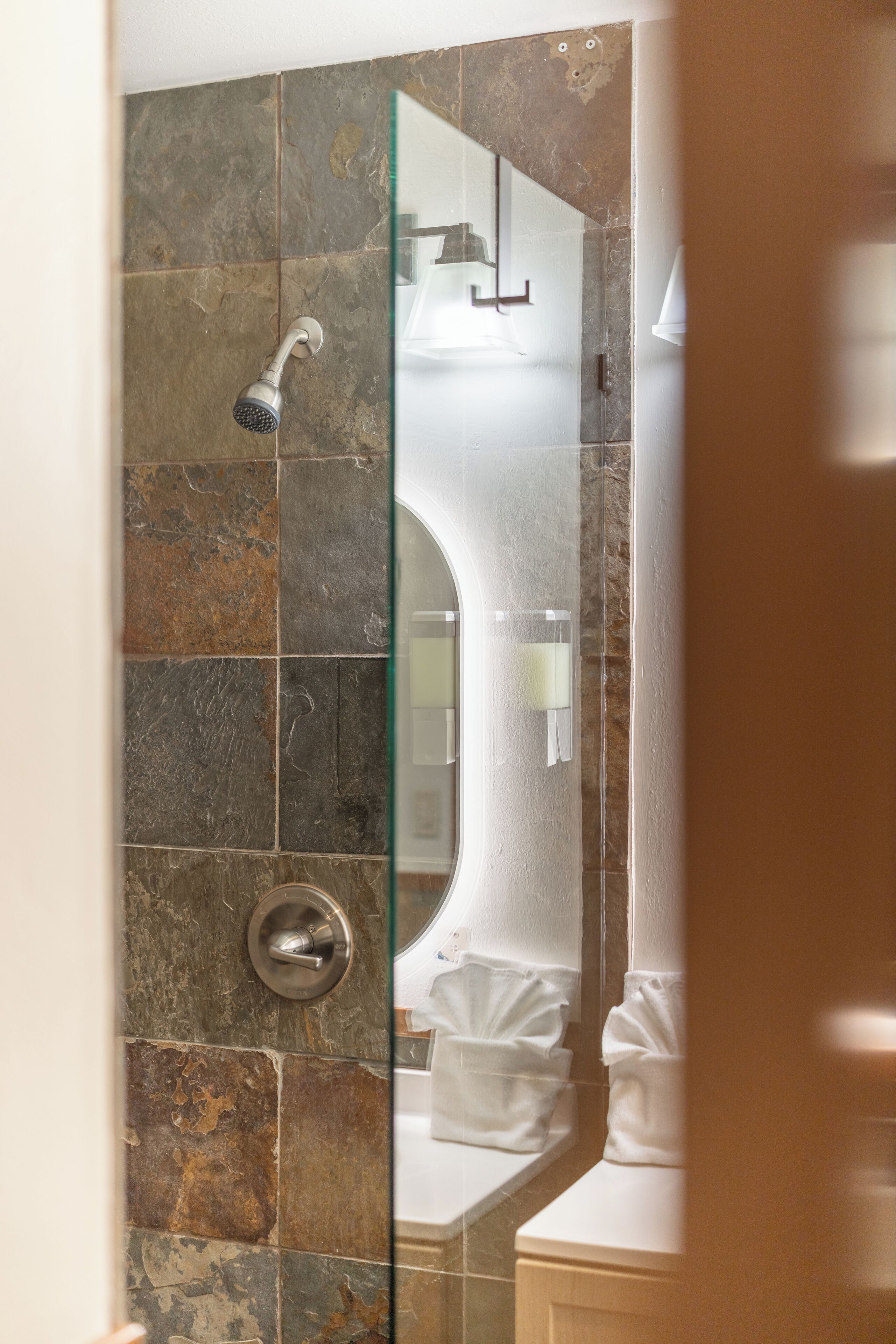 Un bagno con piastrelle in pietra, box doccia in vetro e lavandino bianco.