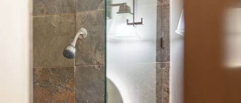 Un baño con baldosas de piedra, cabina de ducha de vidrio y lavamanos blanco.
