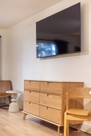 Ein modernes Zimmer mit einem an der Wand befestigten Flachbildfernseher, einem Holfachschrank, einem Holzstuhl und einem kleinen weißen Tisch.