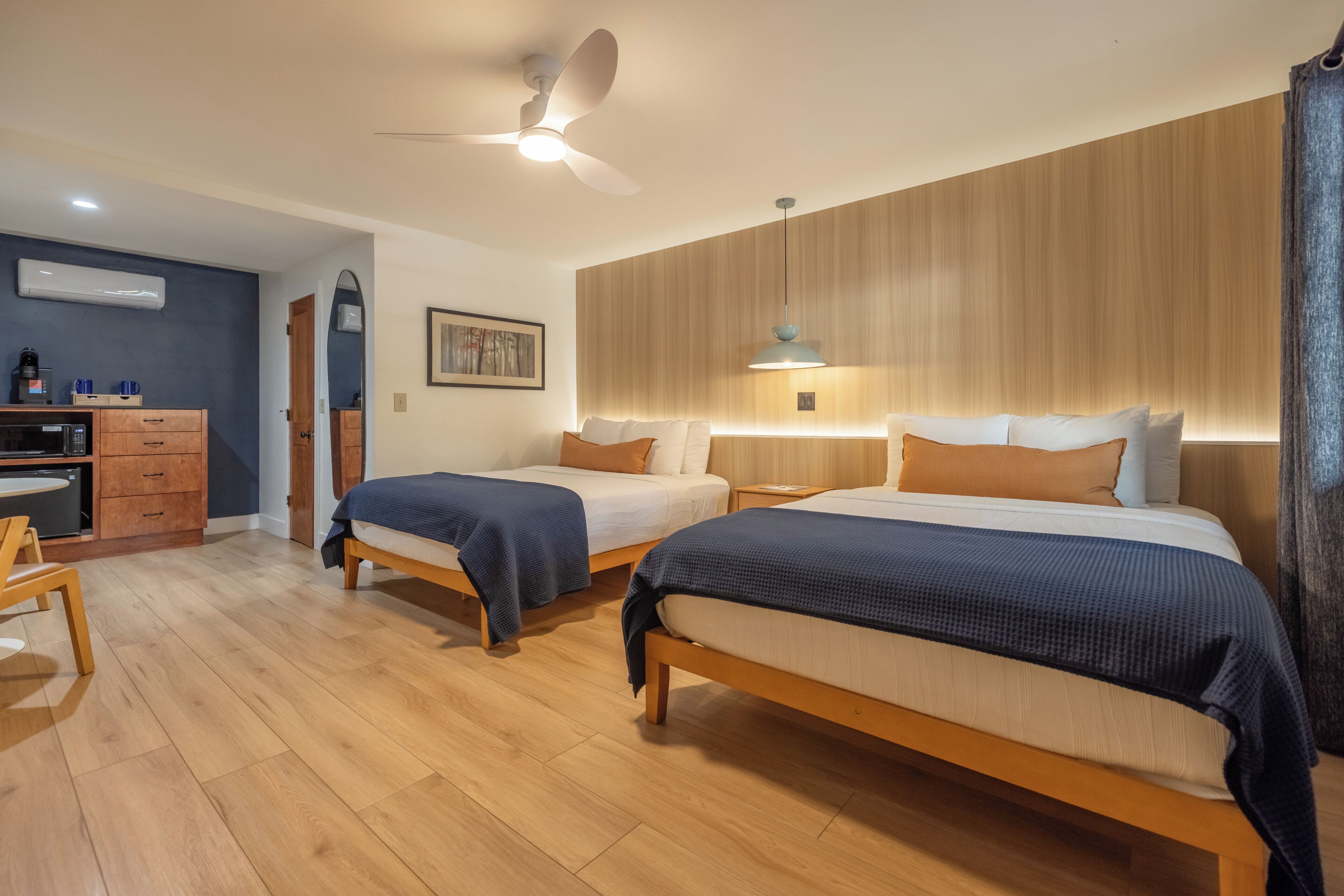 Camera d'albergo con due letti, una scrivania, una sedia, una ventola a soffitto e un condizionatore d'aria a parete.