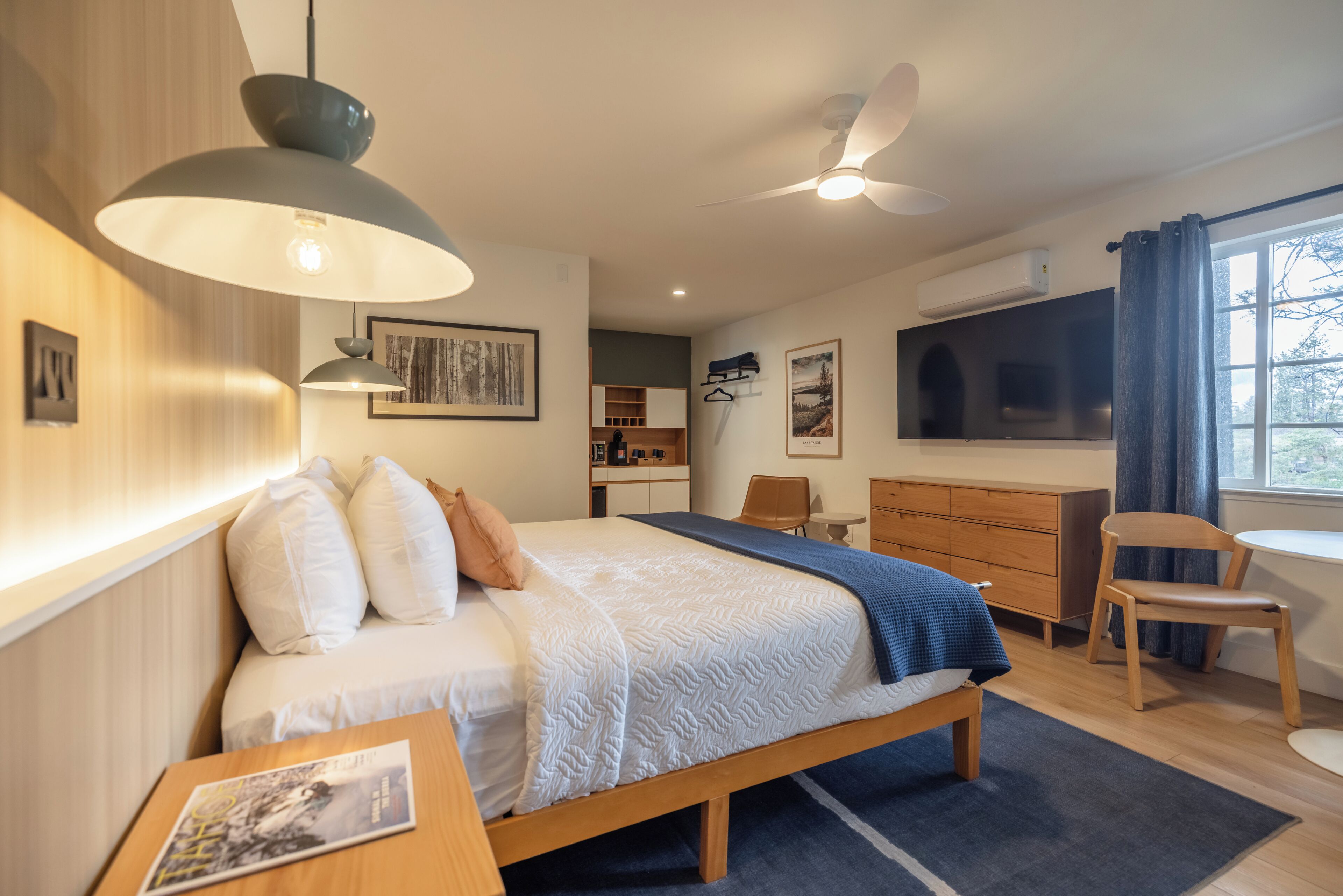 Moderni hotellihuone, jossa on sänky, yöpöytä ja työpöytä tuolilla.