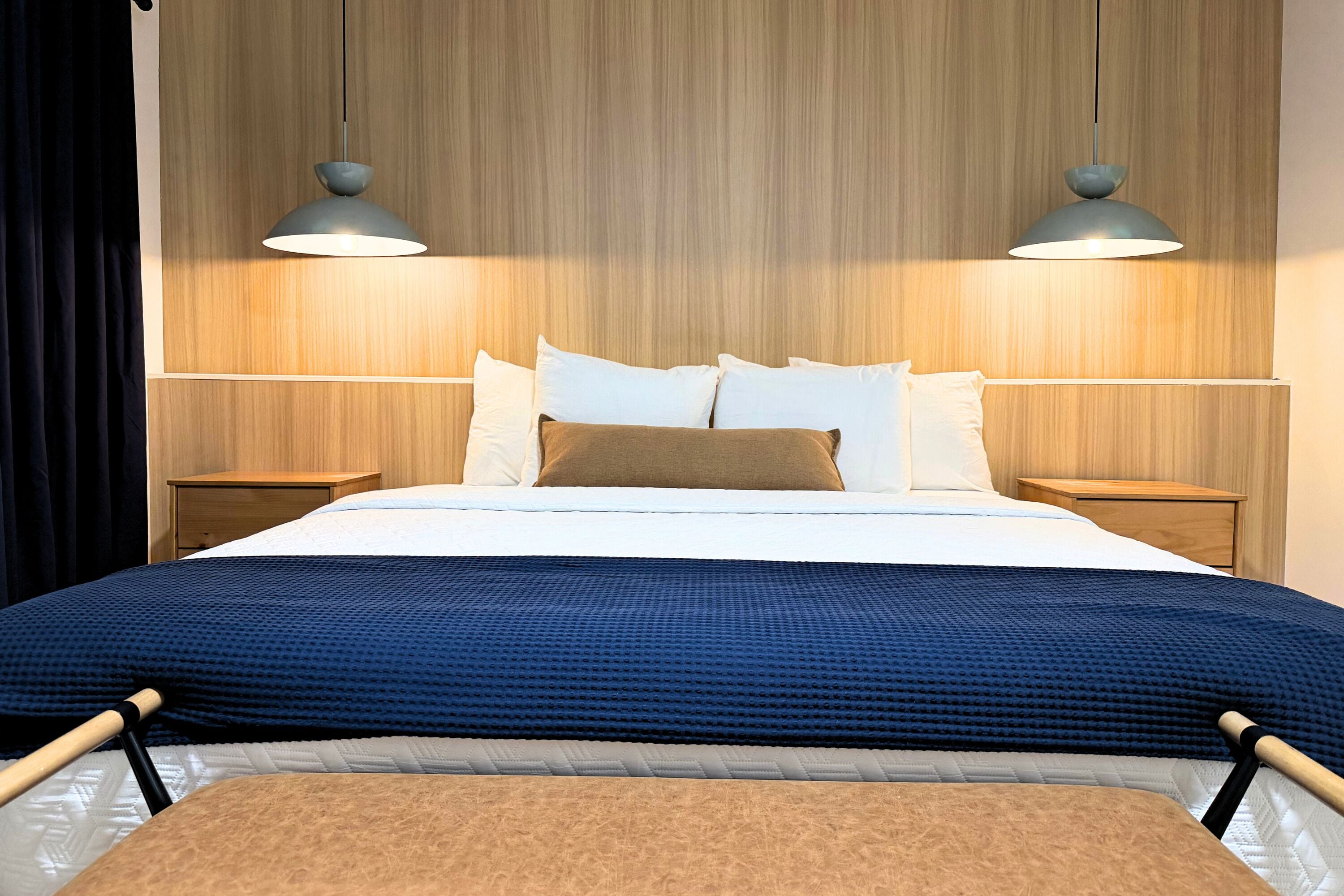 Une chambre d’hôtel avec une tête de lit en bois, un lit avec une literie blanche et marron, deux lampes de chevet et une table de chevet en bois.