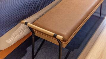 Una cama con colchón azul texturizado, un banco de cuero marrón y patas de metal negro.