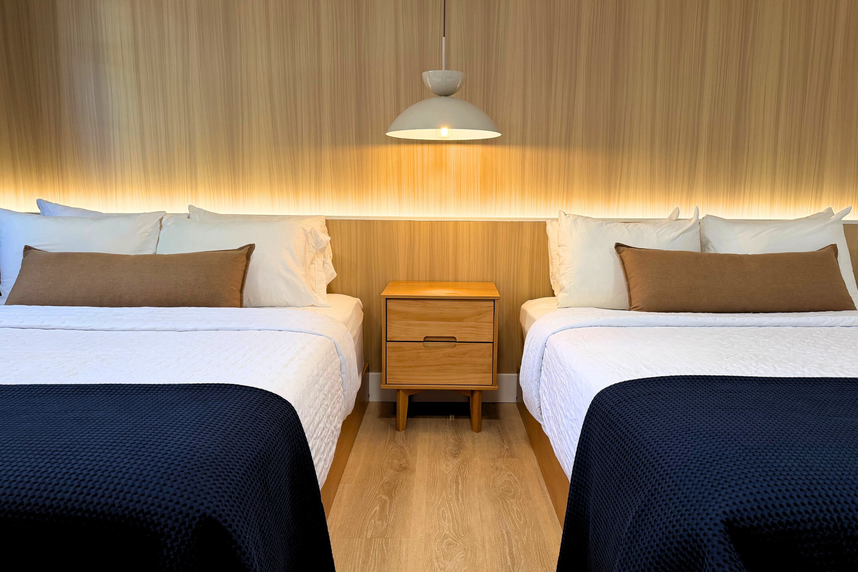 A hotel room with two beds, a wooden nightstand, and a hanging light fixture.