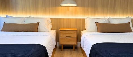 A hotel room with two beds, a wooden nightstand, and a hanging light fixture.