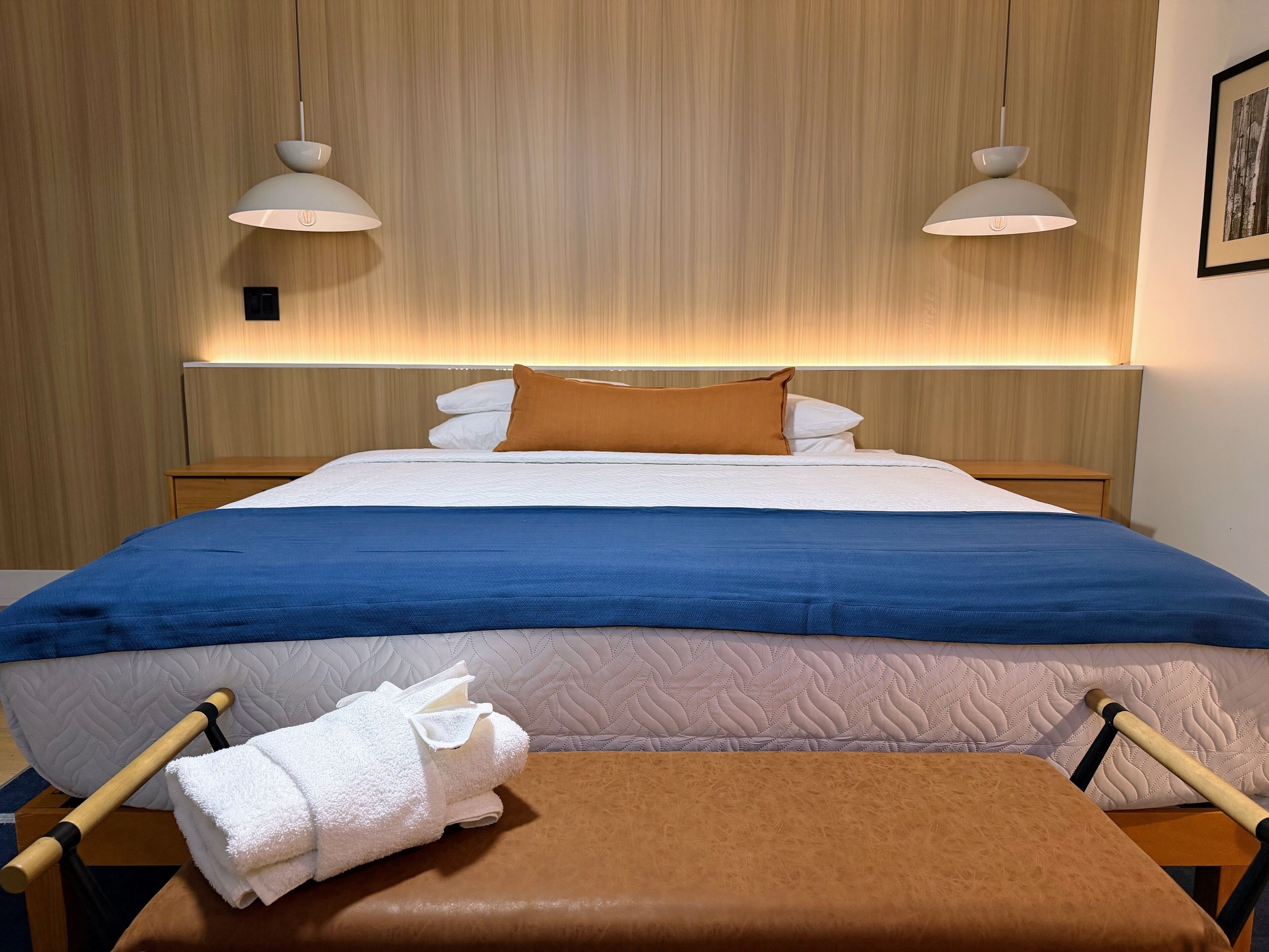 A neatly made bed with a blue and white duvet, a brown pillow, and a white towel on a wooden bench.