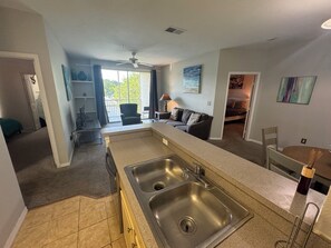 A compact kitchen with a double sink, a dining area with a table and chairs, and a living room with a sofa and a TV.