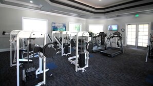 A gym with cardio machines, weight stations, and a TV screen.