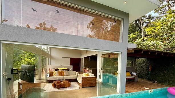 Una casa moderna con un espacio de sala de estar con paredes de vidrio, una piscina y vistas al exterior.