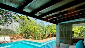 Un área de piscina moderna al aire libre con terraza de madera, sillones de descanso y una zona de estar con vista a la piscina.