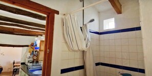 Um banheiro com azulejos brancos e listras azuis, cortina de chuveiro e um vigário de madeira no teto.