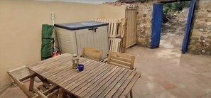 Mesa de madeira com cadeiras, um balde pequeno azul e um armário em ambiente rústico ao ar livre.