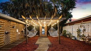 Een houten terras met een pergola erboven, omgeven door rode mulch, dat leidt naar een hangmatgedeelte.