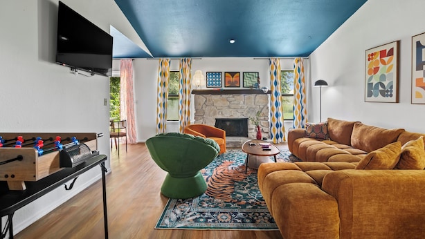 A living room with a foosball table, a green chair, a sofa, a fireplace, and a television on the wall. - Groovy Getaway - Retro Vibes and Modern Comfort (Tulsa)