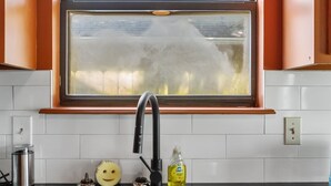 A kitchen with a stainless steel sink, a window with a view of greenery, and a cheerful yellow object on the counter. - Groovy Getaway - Retro Vibes and Modern Comfort (Tulsa)