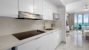 A modern kitchen with white cabinets, a stainless steel sink, and a microwave. There is a balcony with a view of the ocean. - Waterside Historic District Sweeping Views (San Juan)
