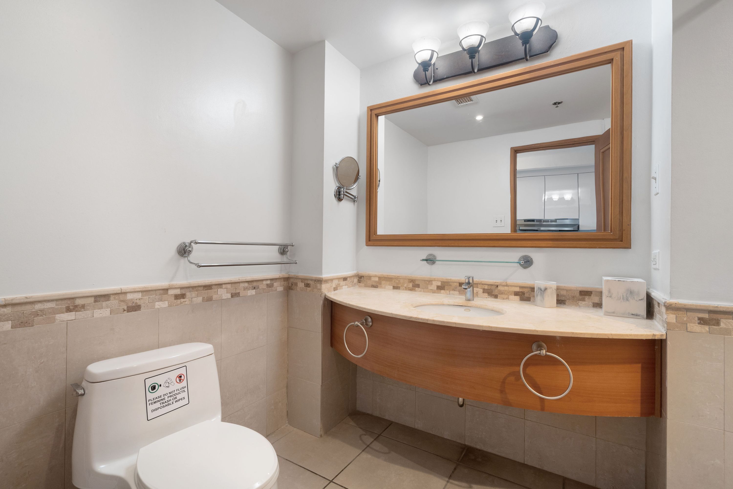 Un baño moderno con inodoro blanco, tocador de madera con dos lavamanos y un espejo grande.